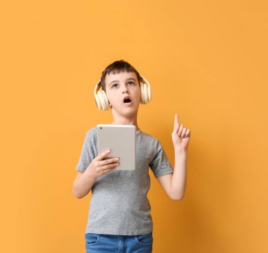 Tablet bilgisayarı ve kulaklıkları olan küçük çocuk renk arkaplanına bir şey gösteriyor.