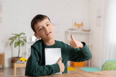 Tabletli küçük çocuk sesli kitap dinliyor ve evde başparmağını kaldırıyor.