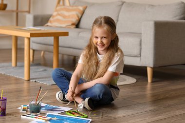 Evde yerde suluboya boyayla resim yapan küçük bir kız.