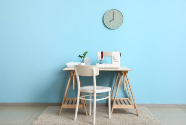 Mavi duvarın yanında dikiş makinesi olan bir terzi.