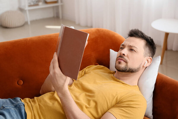 Man with earphones and book lying on sofa