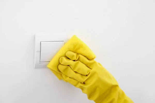 Woman cleaning switch on white wall, closeup