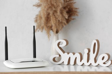 Beyaz duvarın yanındaki masada modern wi-fi yönlendirici ve dekor ögesi