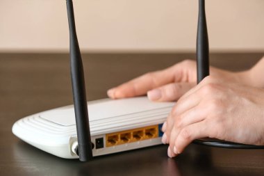 Kadın masadaki kablosuz internet yönlendiricisine ethernet kablosu yerleştiriyor.