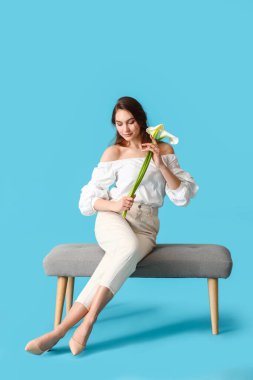 Kalla çiçekleri olan güzel genç bir kadın renk arka planına karşı bankta oturuyor.