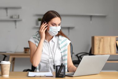 Tıbbi maskeli teknik destek ajanı ofiste çalışıyor.