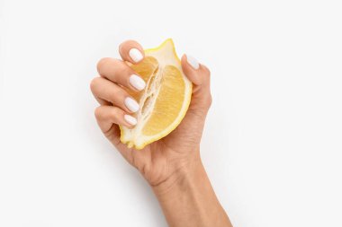 Güzel manikürlü ve beyaz arka planda dilimlenmiş limonlu bir kadın eli.