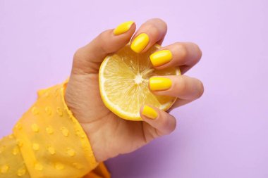 Mor arka planda dilimlenmiş limon tutan modaya uygun manikürlü bir kadın.