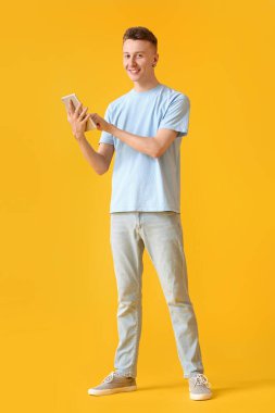 Genç adam sarı arka planda modern tablet bilgisayar kullanıyor.