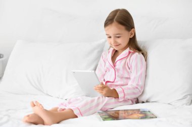 Yatakta tablet bilgisayar kullanan sevimli küçük kız.