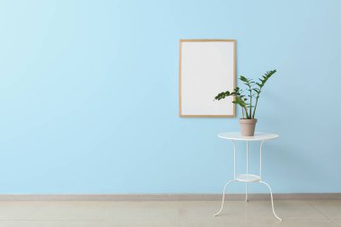 Mavi duvarın yanında boş bir poster çerçevesi ve masa.