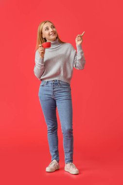 Elinde kahve fincanı olan güzel olgun bir kadın arka plandaki bir şeyi işaret ediyor.