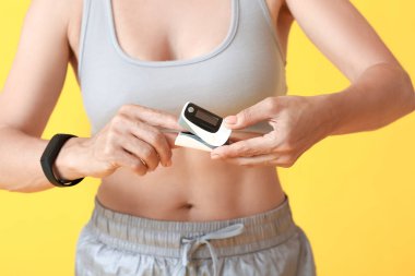 Renk arkaplanında nabız oksimetresi olan kadın koşucu, yakın plan