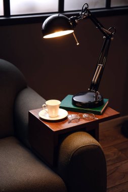 Bardak, gözlük ve lambayla karanlık odada kanepede dikil.