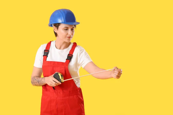 黄色の背景に測定テープとハードハットの女性建設労働者 — ストック写真