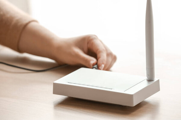 Женщина вставляет провод Ethernet в Wi-Fi маршрутизатор на столе в комнате