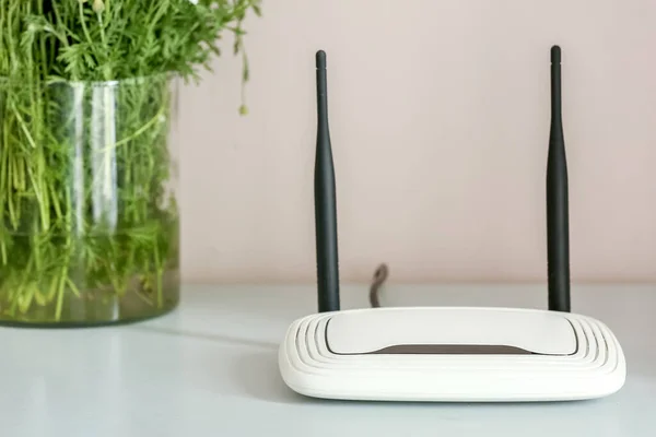 Modern wi-fi router on table near light wall