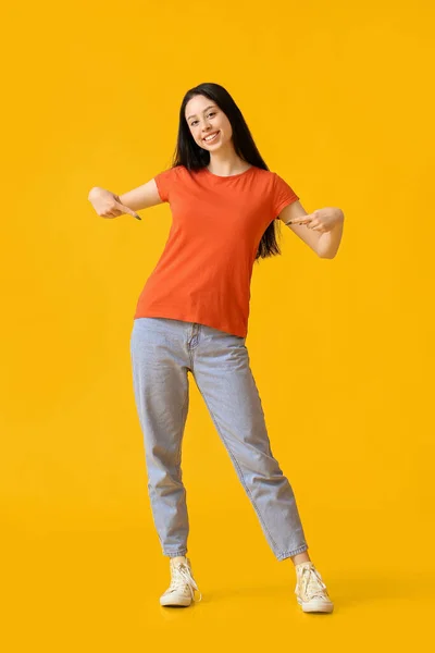 美しいですティーン女の子PointingでオレンジTシャツ上の黄色の背景 — ストック写真