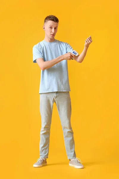 Hombre Joven Con Termómetro Infrarrojo Midiendo Temperatura Sobre Fondo Amarillo — Foto de Stock