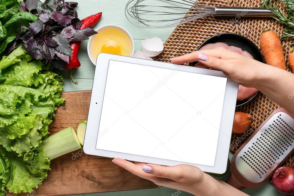 Woman holding digital recipe book and ingredients on color wooden table