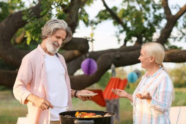 Mutlu yaşlı çift yaz günü barbekü partisinde yemek pişiriyor.