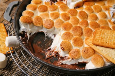 Lezzetli S 'mores soslu kızartma tavası ve ahşap masaya krakerler, yakın plan.
