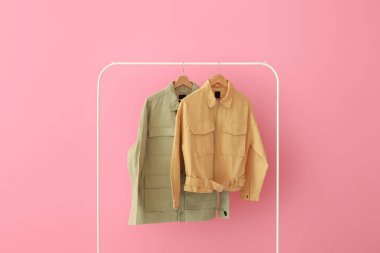 Pembe duvarın yanında yeşil ve sarı ceketli raflar