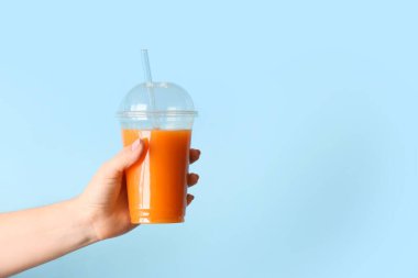 Arka planda plastik bardak sağlıklı meyve suyu olan bir kadın eli.