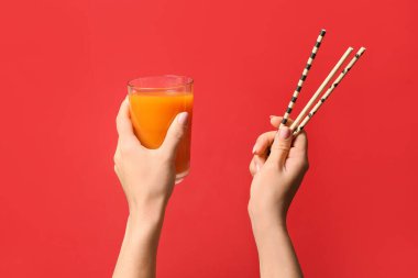 Sağlıklı meyve suyu dolu kadın elleri ve renk arka planında pipetler.