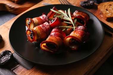 Çıtır pastırma ve ahşap tahtada biberiye dalında pişirilmiş lezzetli kuru erikli siyah tabak.