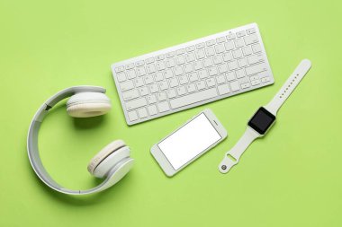 Kulaklık, klavye, cep telefonu ve yeşil arka planda akıllı saat.