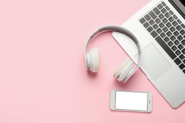 Modern kulaklıklar, cep telefonu ve pembe arka planda dizüstü bilgisayar.