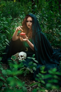 Yeşil ormanda kafatası, mumu ve büyü kitabı olan genç cadı.