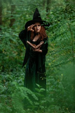 Yeşil ormanda büyü kitabı olan genç cadı.