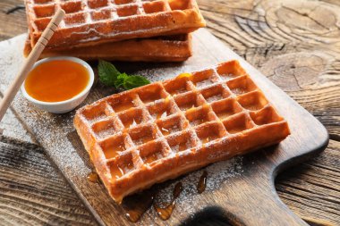 Lezzetli Belçika waffle 'ı ve ahşap arka planda bal olan tahta, yakın plan.
