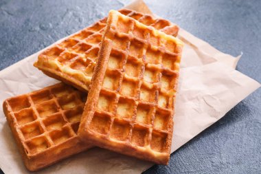 Koyu arkaplanda lezzetli Belçika waffle 'ları olan parşömen, yakın plan.