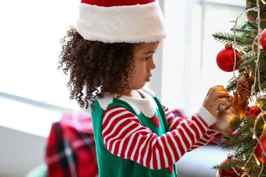 Elf gibi giyinmiş küçük Afro-Amerikalı kız evde Noel ağacı süslüyor.