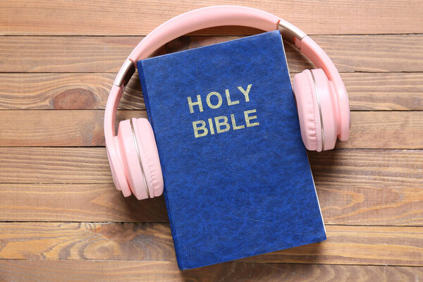 Holy Bible and modern headphones on wooden background