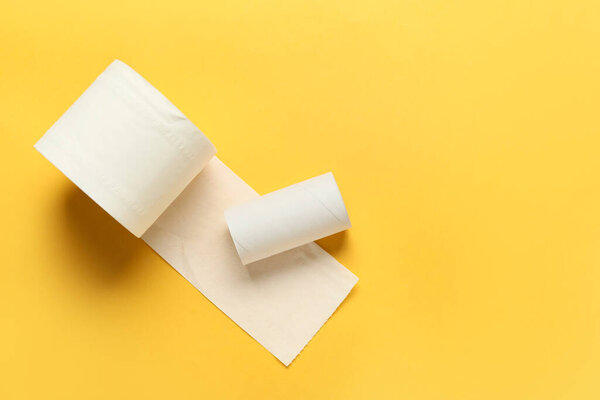 Roll of toilet paper and empty cardboard tube on yellow background