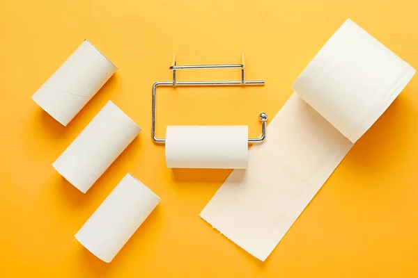 Holder with cardboard tube and toilet paper roll on orange background