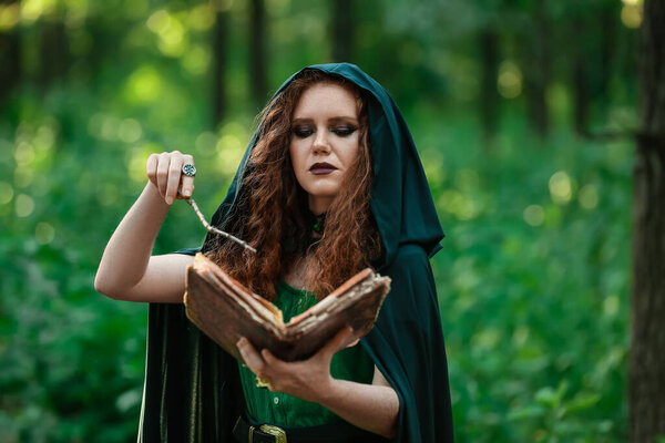 Young witch with spell book in green forest
