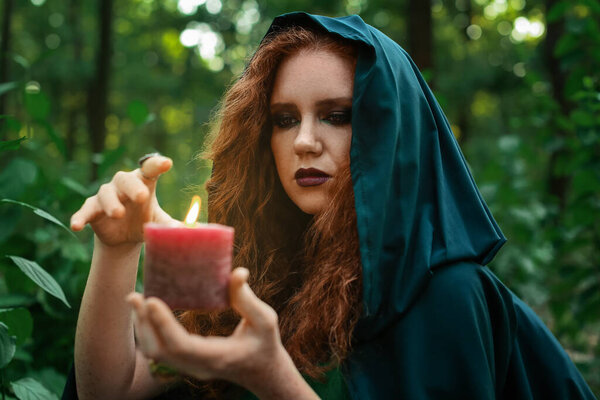 Young witch with candle in green forest