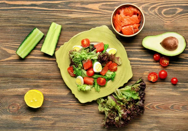 木製の背景にプレートにサーモンと新鮮な野菜とおいしいサラダ — ストック写真