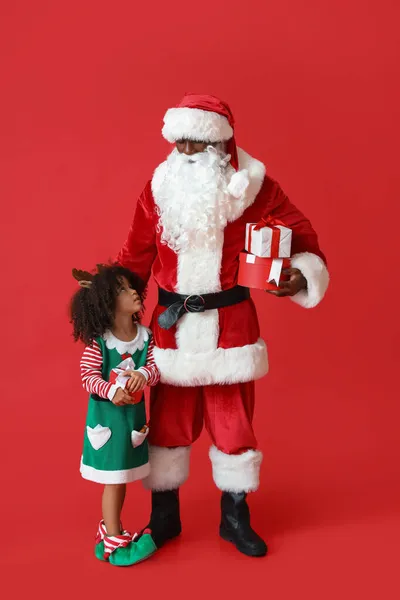 Niedliche Kleine Elfe Mit Weihnachtsmann Und Geschenken Auf Rotem Hintergrund — Stockfoto