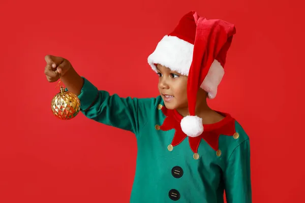 赤の背景にクリスマスボールを持つ小さなアフリカ系アメリカ人の少年 — ストック写真