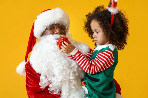 小さなアフリカ系アメリカ人の女の子とともにサンタクロースとクリスマスボール上の黄色の背景 — ストック写真