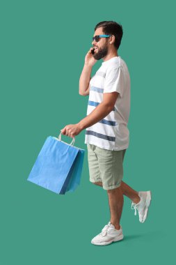 Kara Cuma alışveriş çantalı mutlu genç adam yeşil arka planda cep telefonuyla konuşuyor.