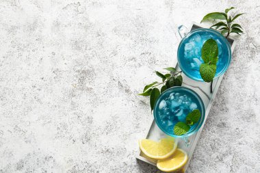 Açık arkaplanda buzlu mavi çay ve limon dolu tahta.