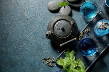 Bir bardak organik mavi çay, kurumuş çiçekler ve koyu arkaplanda nane.