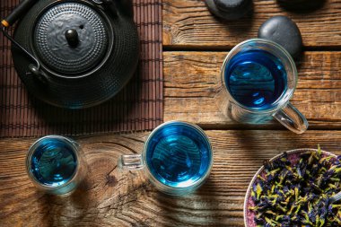 Bir bardak organik mavi çay ve ahşap zemin üzerinde kurumuş çiçekler.